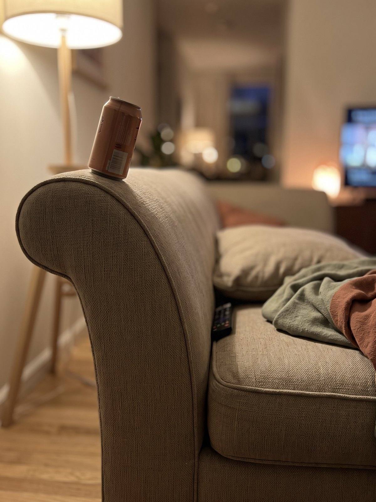 A can balanced on the sloped arm of a couch.