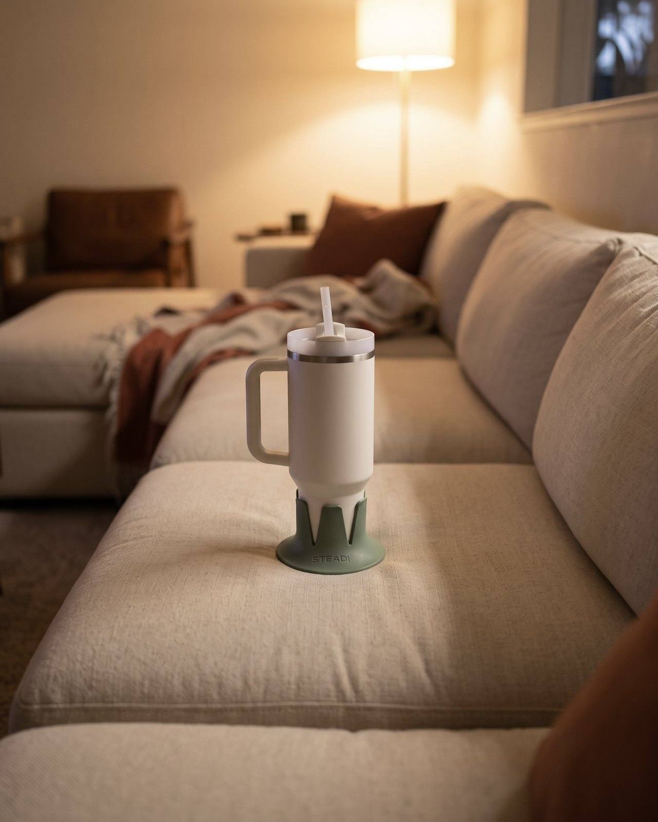 A holder with a tumbler on the middle cushion of a sectional, empty seats on both sides.